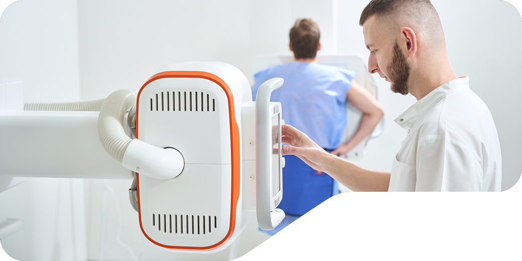 Male healthcare technician operating portable medical ultrasound device with patient in examination room