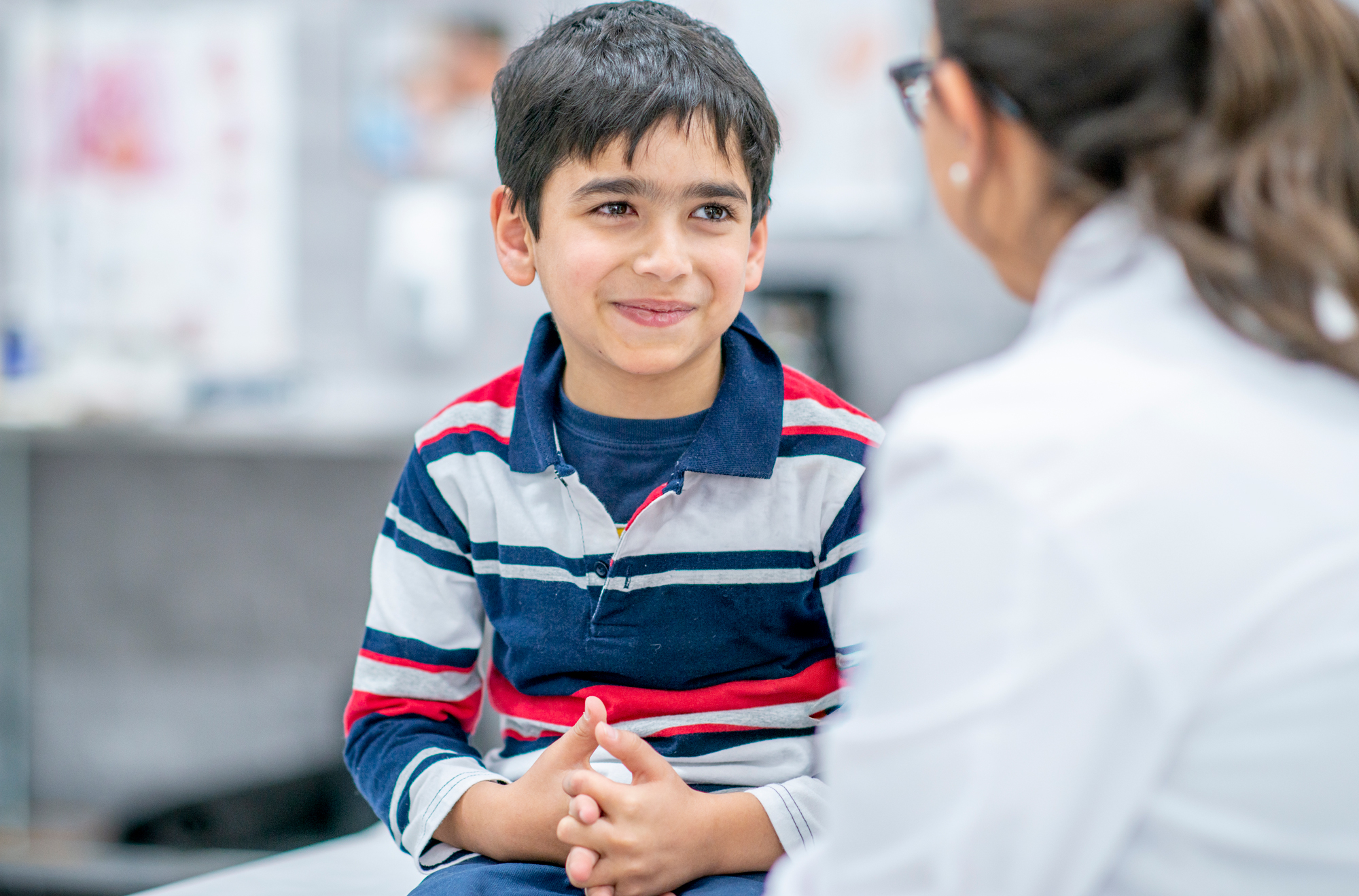 Boy in striped shirt smiling at doctor in medical clinic office