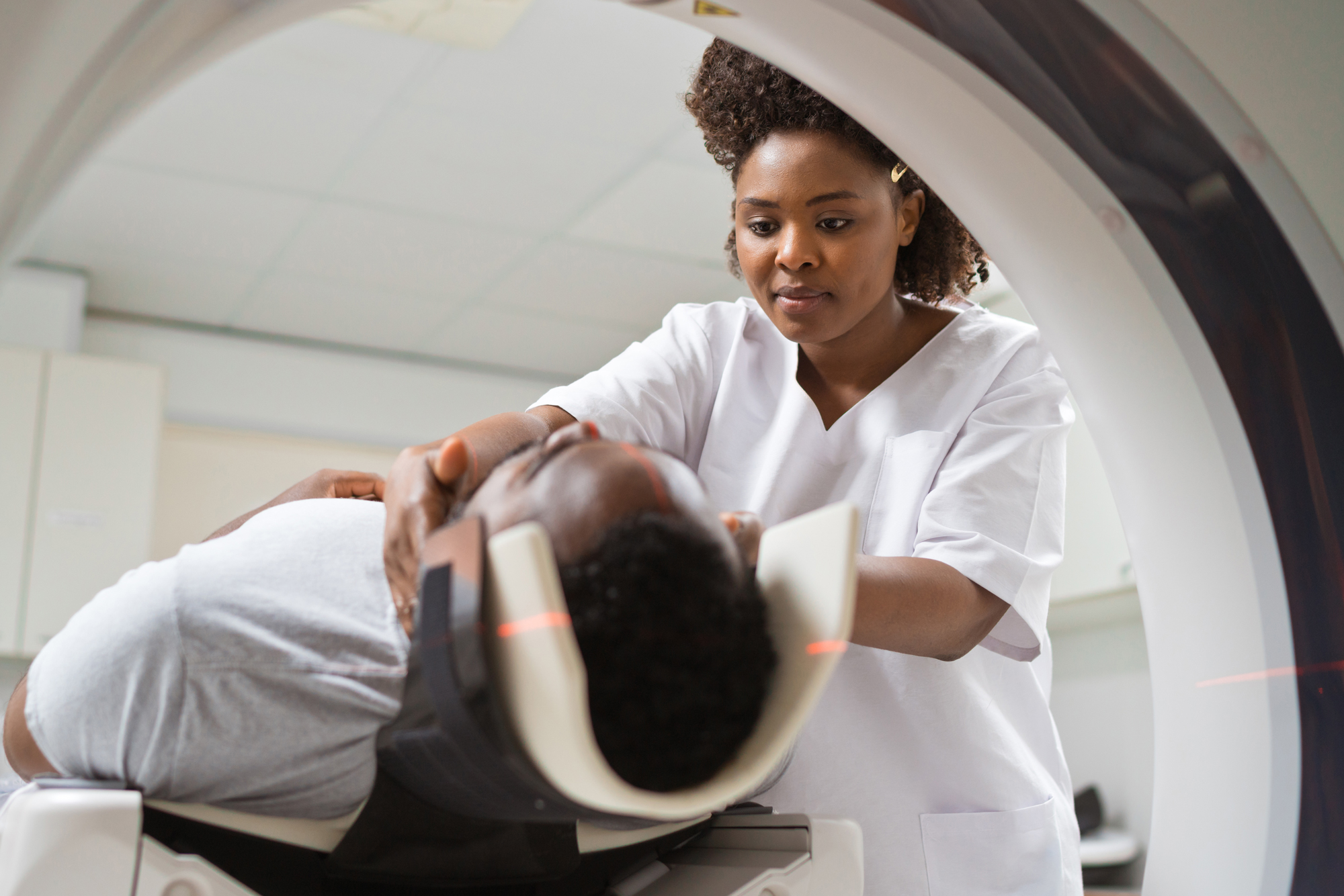 Female radiologic technician in white coat positioning male patient on MRI scanner table in medical imaging center