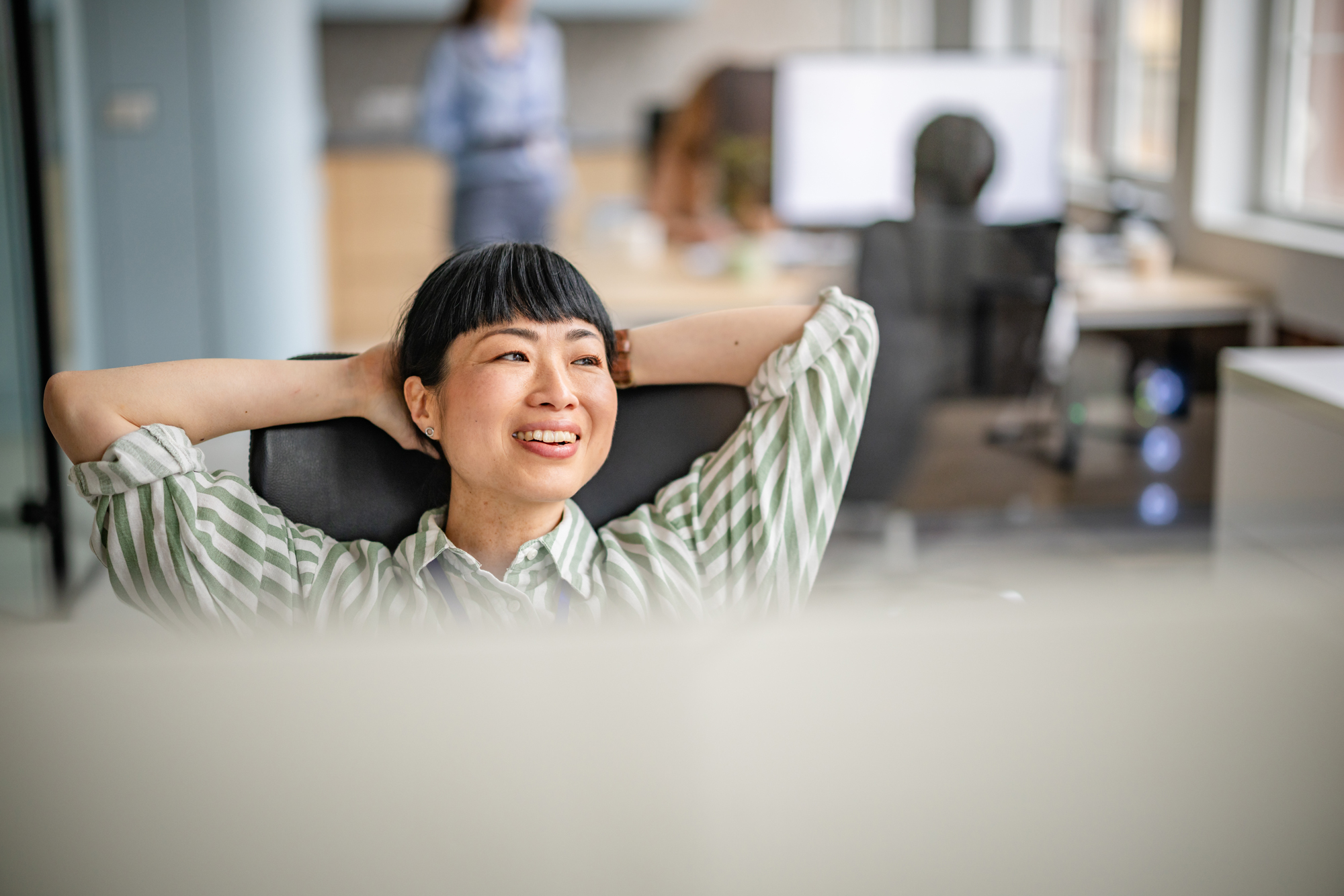 Relaxed woman at office desk leaning back contentedly, representing a healthcare professional freed from IT complexity with radiance365