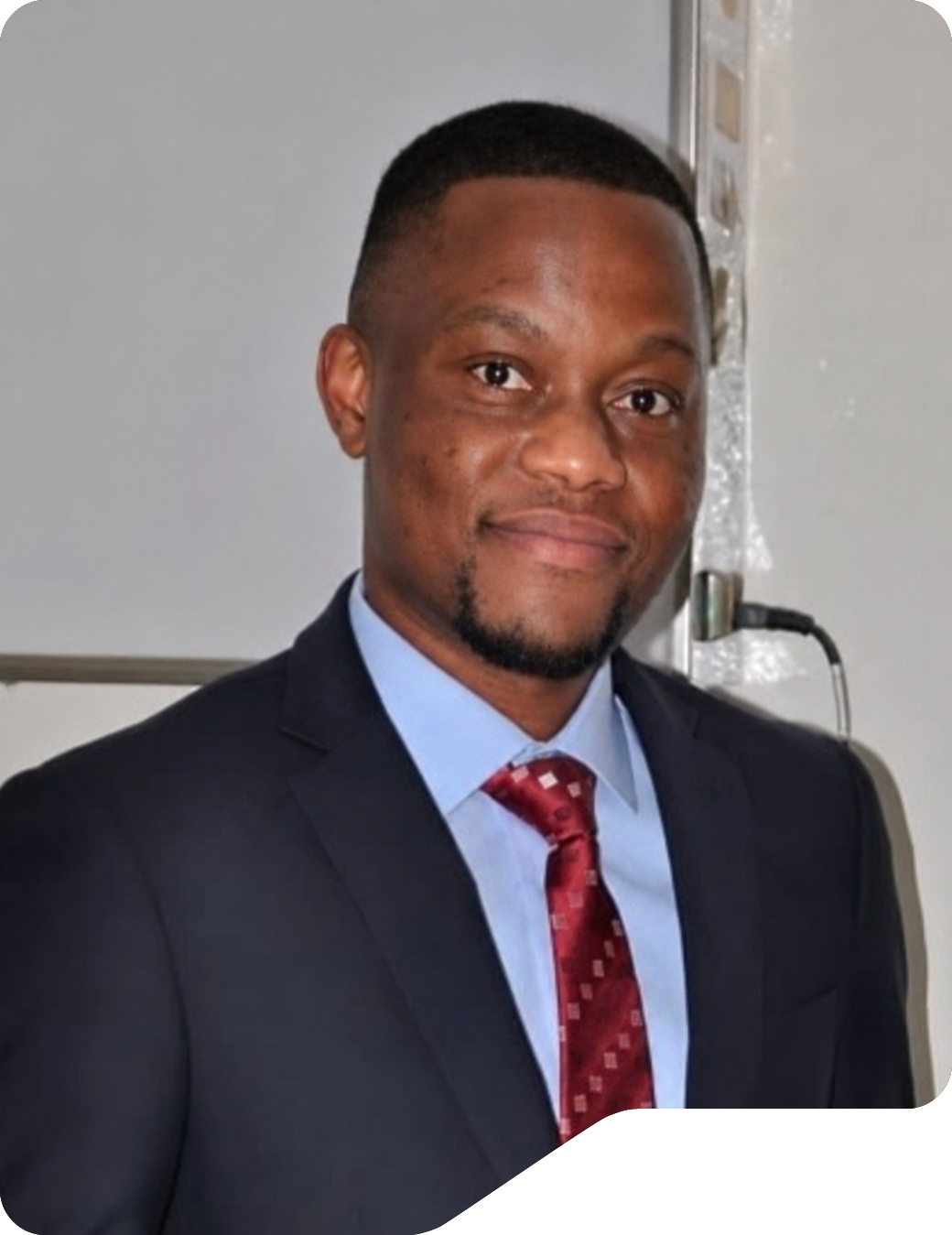 Dr. Axel Kayembe, CEO and founder of TéléradX, smiling in a dark suit, light blue shirt and red tie